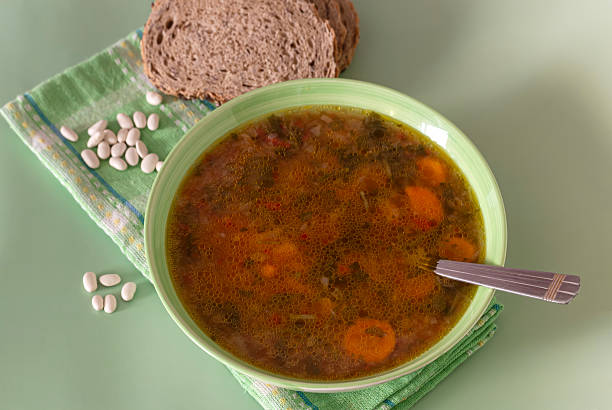 Ready meals. Appetizing, fresh, hot beans soup with celery, carrots and potatoes  in a green bowl close-up