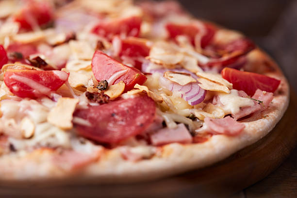 Pizza with ham, salami, cherry tomatoes and mozzarella cheese. Rustic wooden background. Soft focus. Close up.