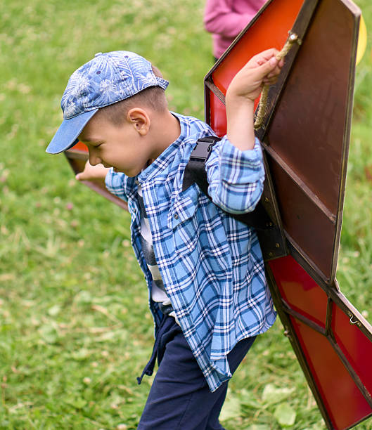 Happy boy is playing with the toy hang glider wings running on a lawn and imagining herself in flight. Shooting at a back yard of country cottage at summer day