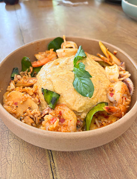 focus on fresh basil leaves placed on top of thai local food ,spicy seafood fried rice mixed with shrimp, squid, vegetables, and chili topped with fluffy eggs omelet served in a brown ceramic plate.