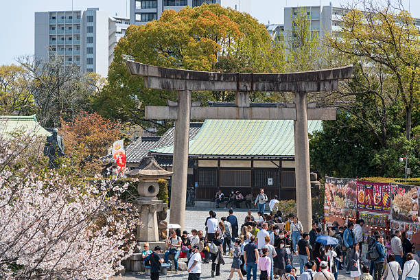 Osaka, Japan - April 8, 2025 : Large crowd visiting the stone torii gate of Hokoku Shrine inside Osaka Castle Park during the cherry blossom season.