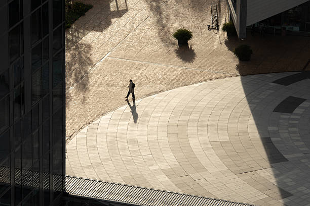 Vilnius, Lithuania - August 27 2025: A solitary person walks through a sunlit urban plaza, casting a long shadow on the patterned ground. The scene captures architectural lines, open space, and minimalism in a city environment