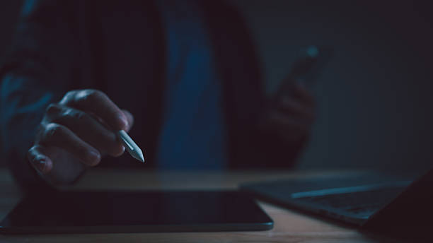 istock Close-up businessman hand holding stylus pen touching tablet screen. Professional creative designer working late night multitasking, using laptop, smartphone. Digital technology, business, 2235180186