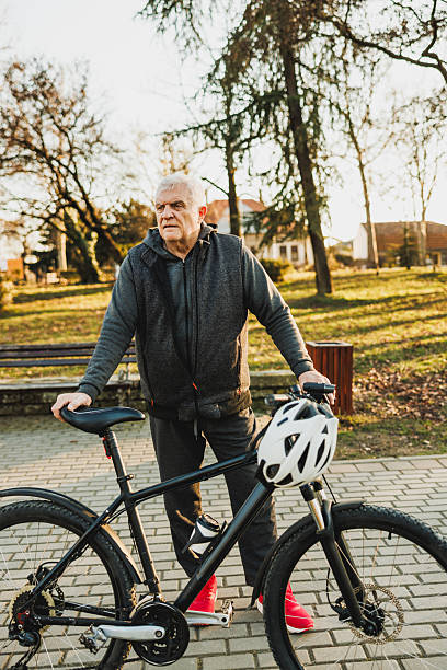 istock Senior Man Holding a Bike on a Paved Park Path 2235180643