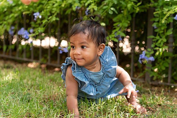 Adorable baby girl crawling on soft grass, joyfully exploring the vibrant garden filled with blooming flowers and lush hedges