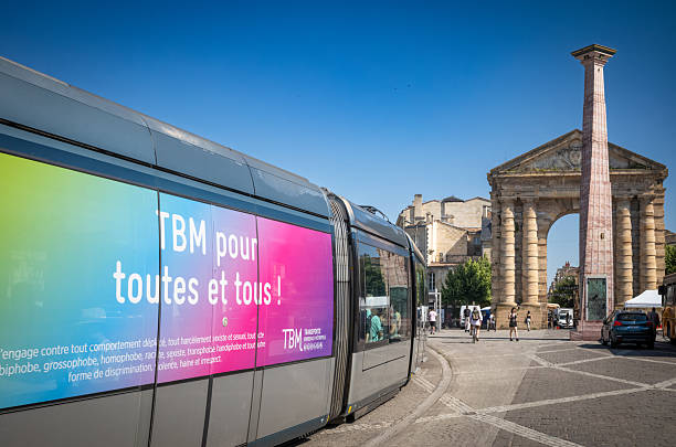 A tram in Place de la Victoire with the slogan TBM is for all passes the 1753 arch Porte d'Aquitaine and the 2005 obelisk designed by Czech artist Ivan Theimer in Bordeaux, France.