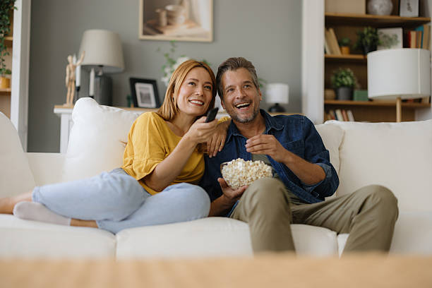 istock Couple relaxing on sofa, watching television and eating popcorn 2235198243