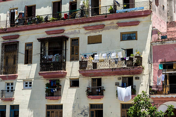 Havan, Cuba-December 2017: Beautiful scenery of a Black woman putting the bedding on the balcony, white sheets fanned on the wind with an old rustic house in the background. Rural tropical cityscape.