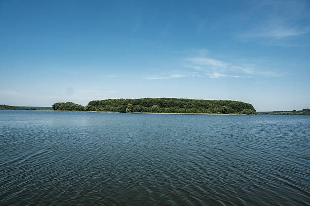 Serene landscape showcases a lush green island nestled in tranquil blue water, with a clear sky above, creating a peaceful atmosphere ideal for nature lovers and outdoor enthusiasts