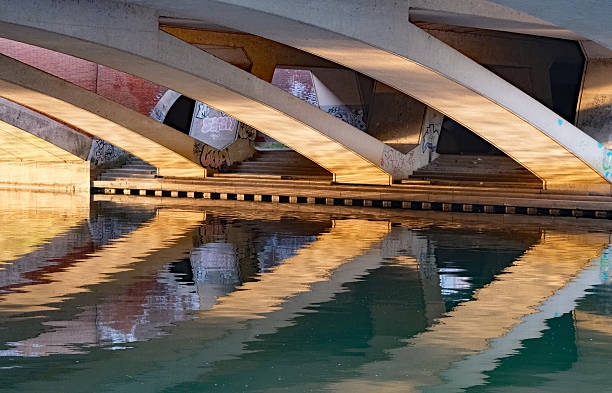 Runnymede, Berkshire, United Kingdom, August 16, 2025. Curved underside of M25 concrete road bridge over the River Thames. Beautiful golden hour reflections and refraction in water. Sunny summer evening outdoors