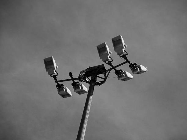 grayscale image of multiple lamps on a high light post in daylight viewed from below