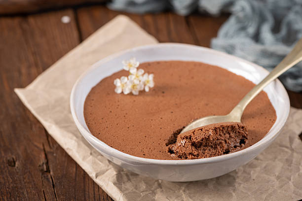 istock Rich dark chocolate mousse in a white bowl, a spoonful lifted, garnished with delicate white flowers, resting on rustic parchment paper and a wooden surface 2235208852