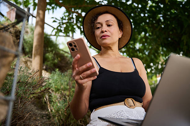 Woman Using Smartphone Outdoors While Working on Laptop in Nature