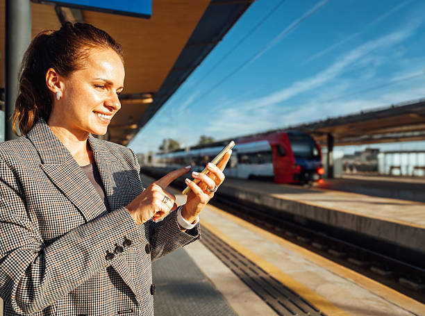 istock Smiling woman commuter checking mobile phone on railroad station platform. 2235220437