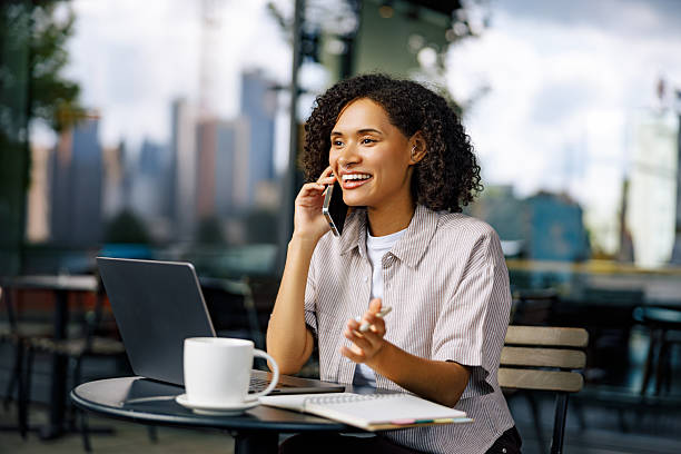 A Woman Engaged in Working on a Laptop while Taking a Phone Call in a Cozy Cafe Setting
