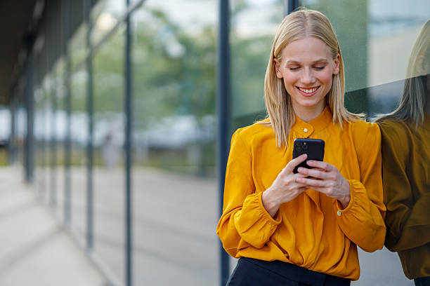 istock Young businesswoman smiling while engaging with her smartphone outside a modern office building, radiating confidence and positivity 2235235465