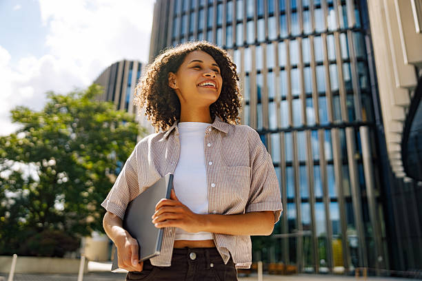 istock A Confident Young Woman is Joyfully Smiling with Her Laptop in a Modern Urban Setting 2235251767