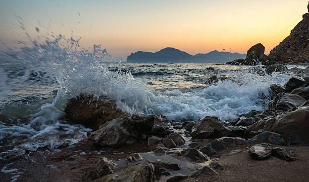istock Powerful sea wave crashing against rocks at sunset 2235255177