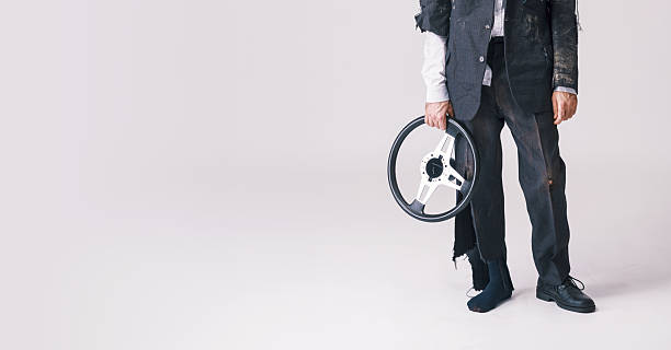 Humorous studio portrait of a man in a ripped suit holding a car steering wheel, representing funny accident, clumsy failure and comic disaster on white background.