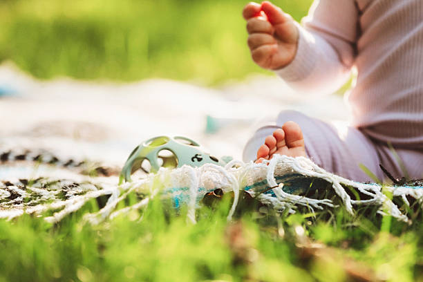 A baby, nine months old, sitting on a blanket outside, playing with a rattle. Shot with a Canon 5D Mark IV.