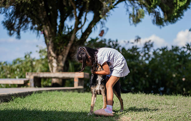 A tender photograph of a little girl affectionately hugging her dog in an outdoor garden. The scene reflects love, trust, friendship, and innocence in the relationship between children and their pets.