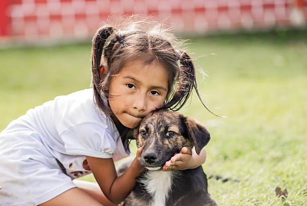 A touching portrait of a girl hugging her dog while sitting on the grass. The image reflects love, innocence, friendship, and the strong bond of trust between children and their pets.