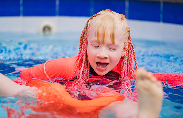 Girl with colorful braids and an orange life jacket playing in the pool. A cheerful and dynamic image that conveys safety, fun, and children's enjoyment of water activities.
