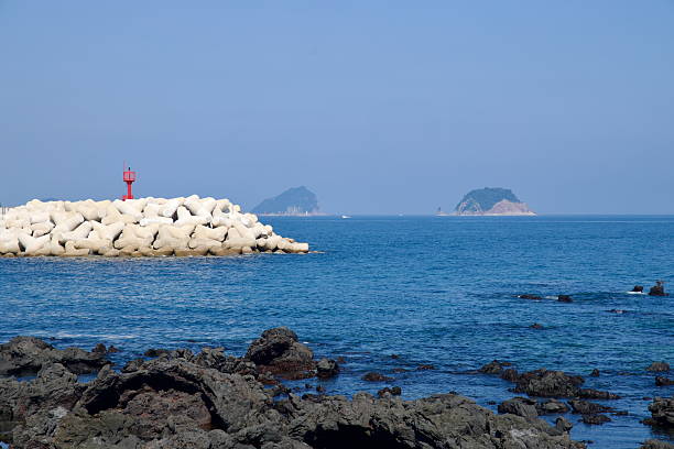 White tetrapods form a breakwater at Beophwan Harbor, with a red lighthouse and the distant silhouettes of Munseom and Beomseom islands across the sea.