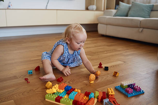 Playful blond girl enjoying the day. Small baby girl playing with blocks indoors.