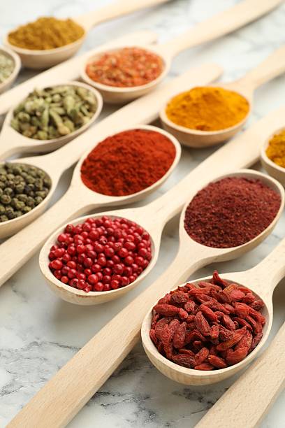 Different aromatic spices in spoons on white marble table, closeup