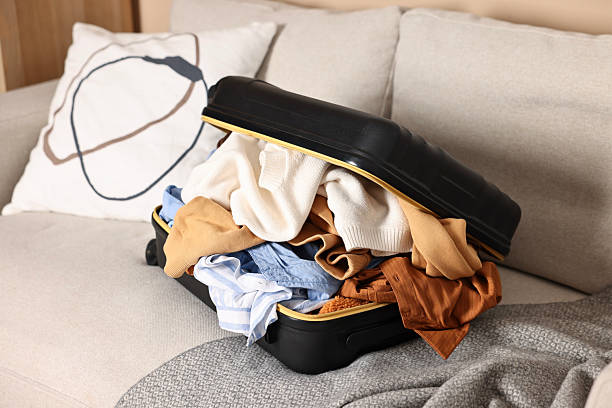 istock Open suitcase full of different messy clothes on sofa indoors 2235322740