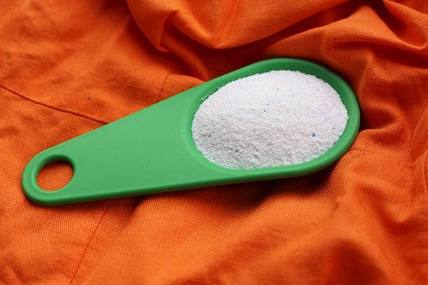 Laundry detergent powder in a green scoop placed on orange fabric.