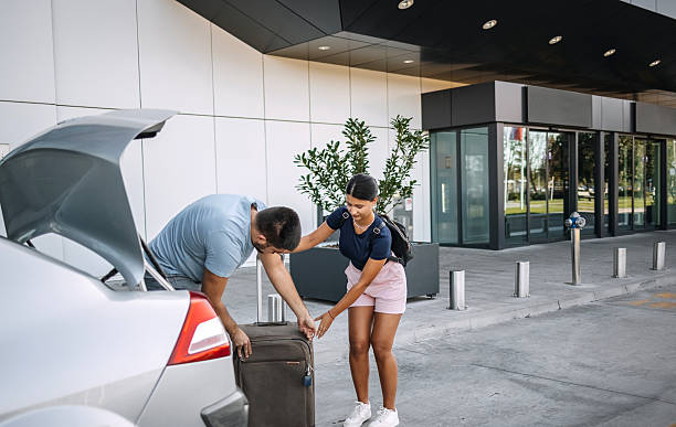 istock Young adults outdoors on sidewalk with suitcase trying to put it in car trunk 2235327200