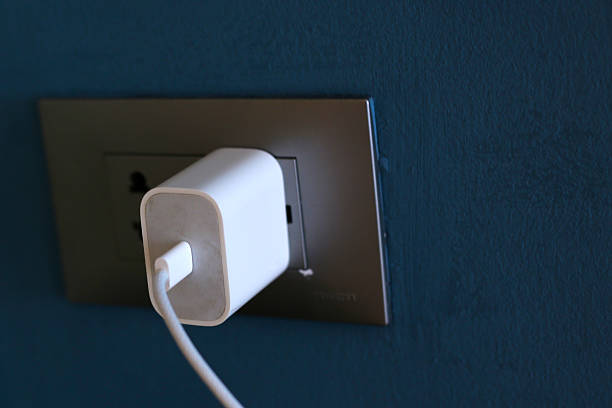 istock : White phone charger plugged into a wall socket with a cable attached. 2235327302