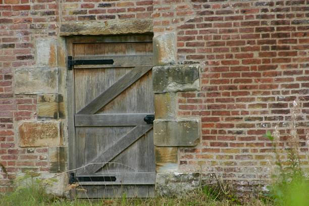 istock A weathered wooden gate is set into a long red brick wall, surrounded by tall grass and wild plants. The scene exudes rustic charm and a sense of quiet, historic countryside seclusion. 2235328055