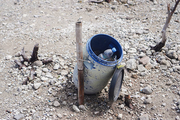 A blue trash bin placed outdoors in an open dusty area.