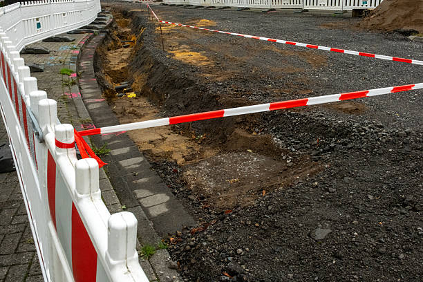 istock Road construction site with barrier tape and open trench 2235332244