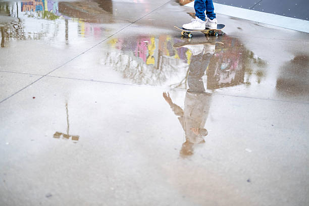 Reflection of young person skateboarding in puddle at skatepark after rain