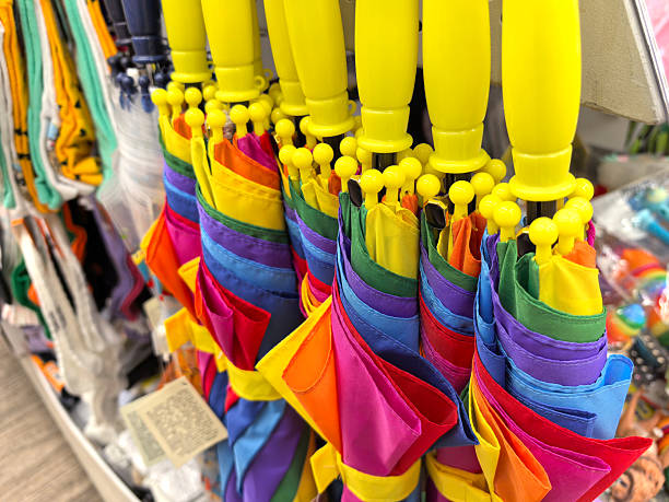 A collection of bright umbrellas with yellow handles hangs in a store, showcasing an array of colors. These playful designs create a cheerful atmosphere, inviting shoppers to brighten their day.