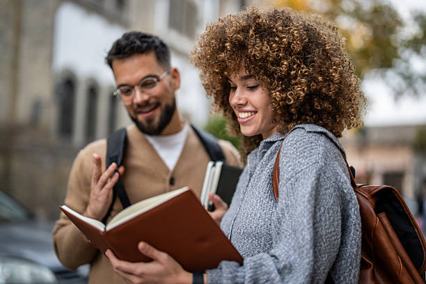 istock Two smiling students reading a book together outdoors 2235351236