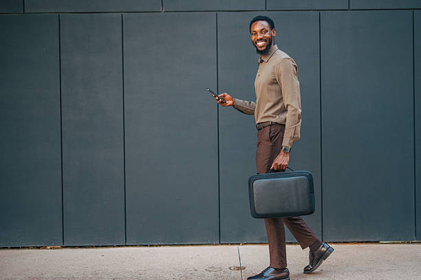 istock Smiling businessman walking and using smartphone in the city 2235354395