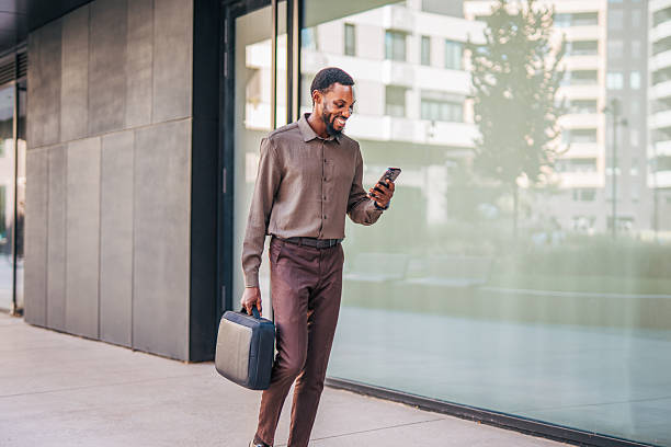 istock Smiling businessman walking and using smartphone in urban setting 2235354421