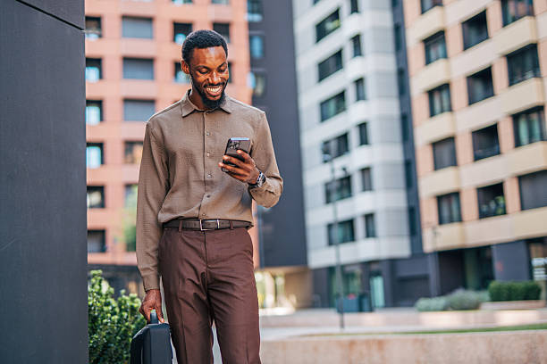 istock Smiling businessman walking and using smartphone in urban setting 2235354484