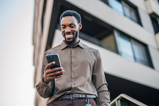 istock Smiling businessman using smartphone in front of modern office building 2235354554