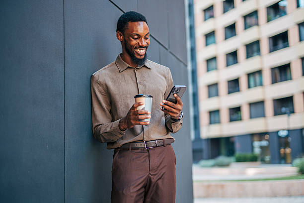 istock Smiling businessman using smartphone and drinking coffee outdoors 2235354644