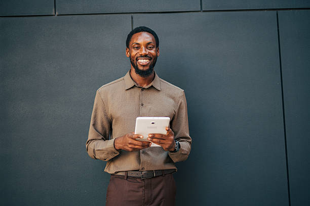 istock Smiling businessman using digital tablet against gray wall 2235355433