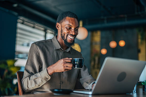istock Smiling young man working on laptop and drinking coffee in cafe 2235355980