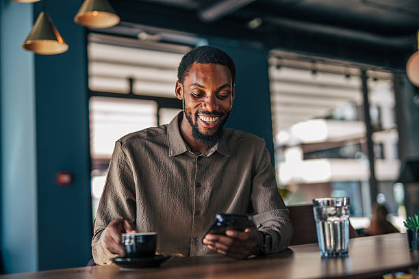 istock Smiling young man using smartphone and drinking coffee in a cafe 2235355985