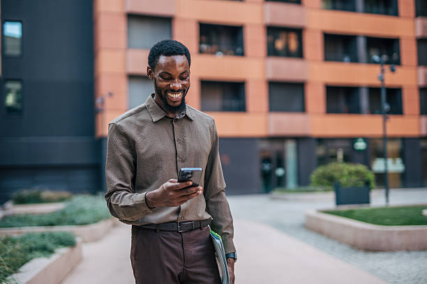 istock Smiling businessman using smartphone while walking outside office building 2235356150