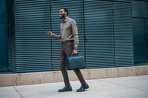 istock Smiling businessman walking and using smartphone near office building 2235356503
